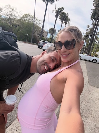 Julieta Puente, embarazada, se toma una selfie con su marido Facundo Miguelena, quien apoya la cabeza en su vientre, en una calle con palmeras