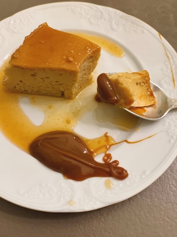 Porción de flan con caramelo, un copo de dulce de leche, y una cuchara con un trozo de flan y dulce de leche sobre un plato blanco
