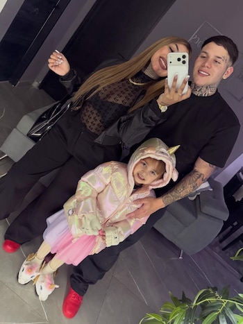 Tamara Báez y Thiago Martínez sonríen mientras posan para una selfie con una niña en el regazo de Thiago, que viste una chaqueta rosa y un vestido. Fondo interior