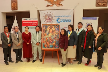 Grupo de personas de pie junto a un cuadro sobre un caballete con la imagen de la Virgen de la Candelaria frente a carteles institucionales