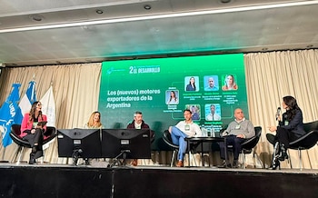 Seis personas sentadas en un escenario durante una conferencia, con una pantalla verde al fondo mostrando el título del evento y los nombres de los panelistas