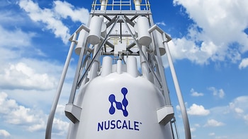 Una estructura cilíndrica blanca con el logotipo azul de NuScale ante un cielo azul con nubes