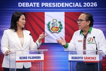 Keiko Fujimori en saco blanco y Roberto Sánchez en camisa blanca con detalles verdes y étnicos, debaten en podios transparentes ante la bandera de Perú.