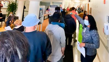 In this photo provided by The Mendocino Voice, a health care worker directs people lined up in the Adventist Health Ukiah Valley Medical Center, Monday, Jan. 4, 2021, in Ukiah, Calif., to get the Moderna COVID-19 vaccination during an emergency vaccine drive. A power failure for the freezer holding the county's ration of the Moderna vaccines forced the emergency distribution of 850 doses of that vaccine. (Jethro Bowers/The Mendocino Voice via AP)