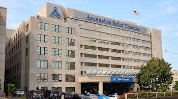 Fachada de un edificio gris de varios pisos con el letrero Ascension Saint Thomas, cartel de entrada principal y automóviles.
