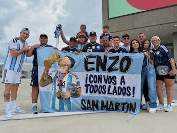 Un grupo de once personas, incluyendo niños, sostiene una bandera celeste y blanca con la imagen de un jugador de fútbol y el texto Enzo, San Martin