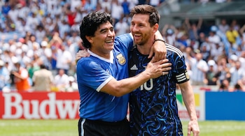 Diego Maradona y Lionel Messi abrazados en un campo de fútbol con público borroso, Maradona con camiseta azul y Messi con camiseta oscura.