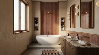Vista de un baño moderno con una bañera blanca exenta, doble lavabo con encimeras de mármol marrón, gabinetes de madera oscura, paredes de azulejos rojizos y un gran ventanal.