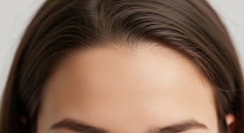 Primer plano de la frente de una mujer con cabello castaño oscuro, cejas marcadas y piel clara. Se aprecian pequeños vellos en la línea de nacimiento del cabello.