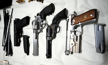 Una vista superior de cuatro armas cortas de fuego, que incluyen dos pistolas y dos revólveres, municiones y precintos de plástico, dispuestas sobre una superficie blanca