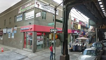 Edificio de ladrillo con letreros comerciales, una sucursal bancaria en la esquina, peatones, vehículos y una vía de tren elevado