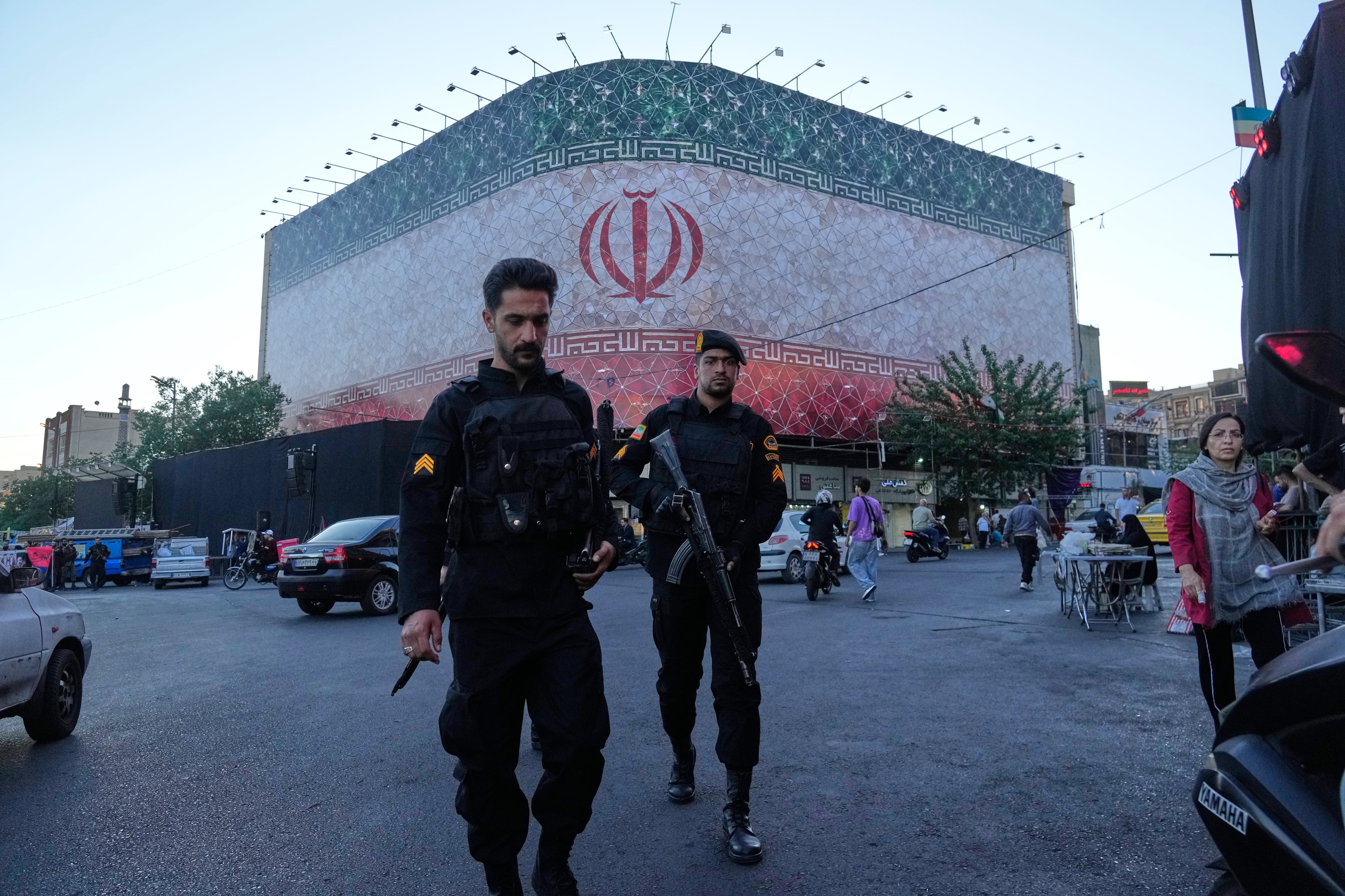 Policías caminan frente a una enorme pancarta con la bandera iraní en la plaza de la Revolución Islámica en Teherán, Irán, el domingo 14 de junio de 2026
(Foto AP/Vahid Salemi)