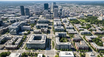 Vista aérea de una ciudad con rascacielos, edificios de oficinas, bloques residenciales, calles con vehículos y parques urbanos con árboles.