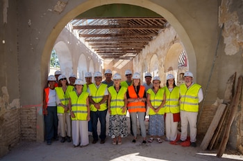Grupo de personas con chalecos reflectantes y cascos de seguridad posa en el interior de una nave en restauración durante una visita a las obras del Monasterio de San Isidoro del Campo, en Santiponce, relacionadas con un hallazgo arqueológico reciente.