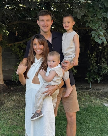 Retrato familiar de Laura Urruticoechea, su esposo y sus dos hijos pequeños sonriendo al aire libre con vegetación y un muro de fondo