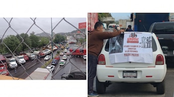 Carretera con tráfico de camiones y coches vista a través de una reja. Hombre coloca pancarta de AMOTAC con mensaje anticorrupción en coche.