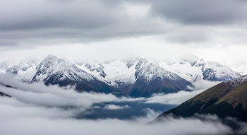 Vista panorámica de la Cordillera de los Andes con montañas nevadas, nubes grises en el cielo y niebla densa cubriendo parcialmente los valles y laderas.