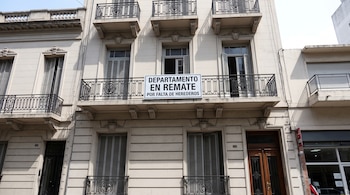 Fachada de un edificio con balcones de hierro y un cartel con la leyenda DEPARTAMENTO EN REMATE POR FALTA DE HEREDEROS.
