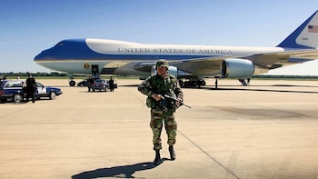 Un soldado armado camina por la pista de aterrizaje frente al avión Air Force One y dos automóviles estacionados