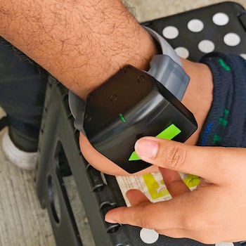 Primer plano del antebrazo y la muñeca de una persona con un dispositivo de seguridad electrónico negro y gris de H&M; otra mano lo manipula