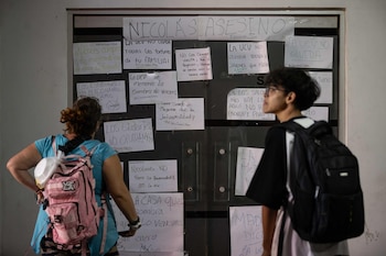 Dos personas observan una pared cubierta con múltiples carteles de protesta manuscritos que incluyen mensajes contra Nicolás Maduro y reclamos estudiantiles