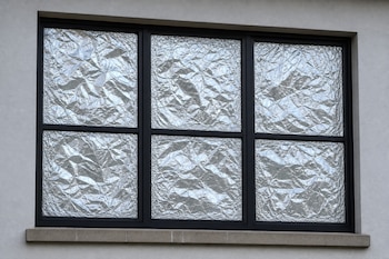 Una ventana de marco negro con tres secciones cuyas superficies de vidrio están totalmente cubiertas con papel de aluminio arrugado.