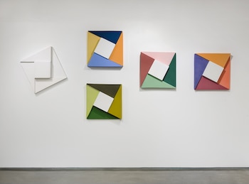 Cinco obras de arte abstracto geométrico cuelgan en una pared blanca. Una es completamente blanca; las otras cuatro tienen formas coloridas con un centro blanco