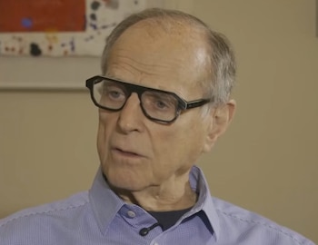 Retrato de Alan Rothenberg, un hombre de edad avanzada con gafas de pasta negra y camisa azul a cuadros