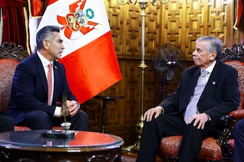 Fernando Rospigliosi y Alejandro Moreno, vestidos de traje, sentados frente a frente en sillones rojos, con la bandera de Perú y una pared de madera tallada de fondo
