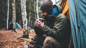 Un aventurero preparando su carpa en una zona de camping rodeada de montañas nevadas, cerca de un lago y un río. La imagen captura el espíritu del turismo de aventura y las vacaciones en entornos naturales, donde la preparación para el frío es esencial. Ilustra la conexión entre el ser humano y la naturaleza, y la búsqueda de experiencias únicas lejos del bullicio urbano. (Imagen ilustrativa Infobae)