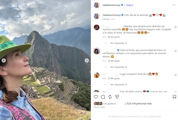 Natalia Oreiro con sombrero verde y camisa estampada azul y rosa mira hacia arriba. Ruinas de piedra y montañas bajo un cielo nublado al fondo