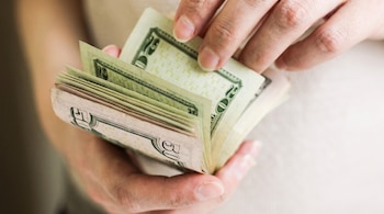 Primer plano de dos manos sujetando y contando billetes de veinte y cincuenta dólares estadounidenses.