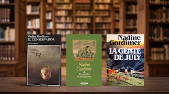 Tres libros de Nadine Gordimer: El Conservador, Un capricho de la naturaleza y La gente de July, sobre una mesa frente a estanterías con libros.