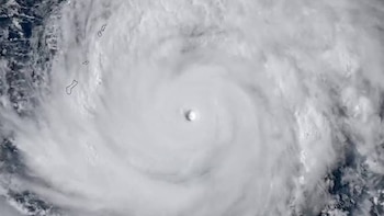Vista satelital de un gran super tifón blanco con un ojo central claro, rodeado de nubes en espiral sobre el océano oscuro. Se observan contornos de islas a la izquierda