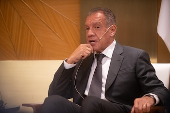 Daniel Hadad viste traje oscuro, camisa blanca y corbata, y lleva un micrófono mientras permanece sentado en un sillón
