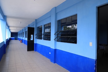 Pasillo largo y vacío de un edificio escolar con paredes pintadas de azul claro y azul oscuro, ventanas enrejadas y un piso de baldosas claras