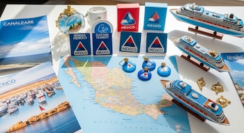 Mapa de México, tres modelos de cruceros, folletos, souvenirs con logos de compañías, tazas, reloj y varios llaveros sobre una mesa blanca.