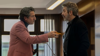 Dos hombres, Diego Peretti y Ricardo Darín, en una conversación intensa. Peretti, con saco rosa, gesticula con un bolígrafo naranja hacia Darín