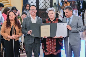 Cuatro personas de pie en primer plano. Dos hombres y dos mujeres. Un hombre y una mujer sostienen una carpeta abierta con documentos. Dos personas usan bastones blancos