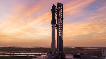 Cohete Starship de SpaceX y torre de lanzamiento en la base Starbase al atardecer, con agua y vegetación en el horizonte