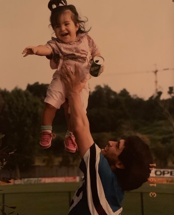 Diego Maradona sostiene en alto a su hija pequeña, quien lleva una lata de bebida en la mano, en un campo al aire libre