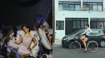 Mujer con vestido rosa y boa blanca canta en escenario; otra mujer en bicicleta junto a coche gris y edificio blanco con número 1409, y cartel de venta.