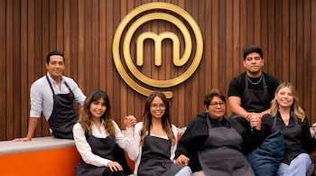 Seis personas, tres mujeres y tres hombres, con mandiles negros de chef, sentados frente a un gran logo dorado de MasterChef sobre una pared de madera.