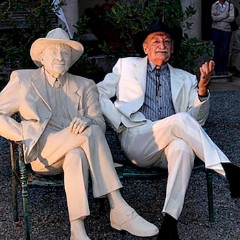 René Lavand con traje y sombrero sentado en un banco junto a una escultura blanca de aspecto idéntico