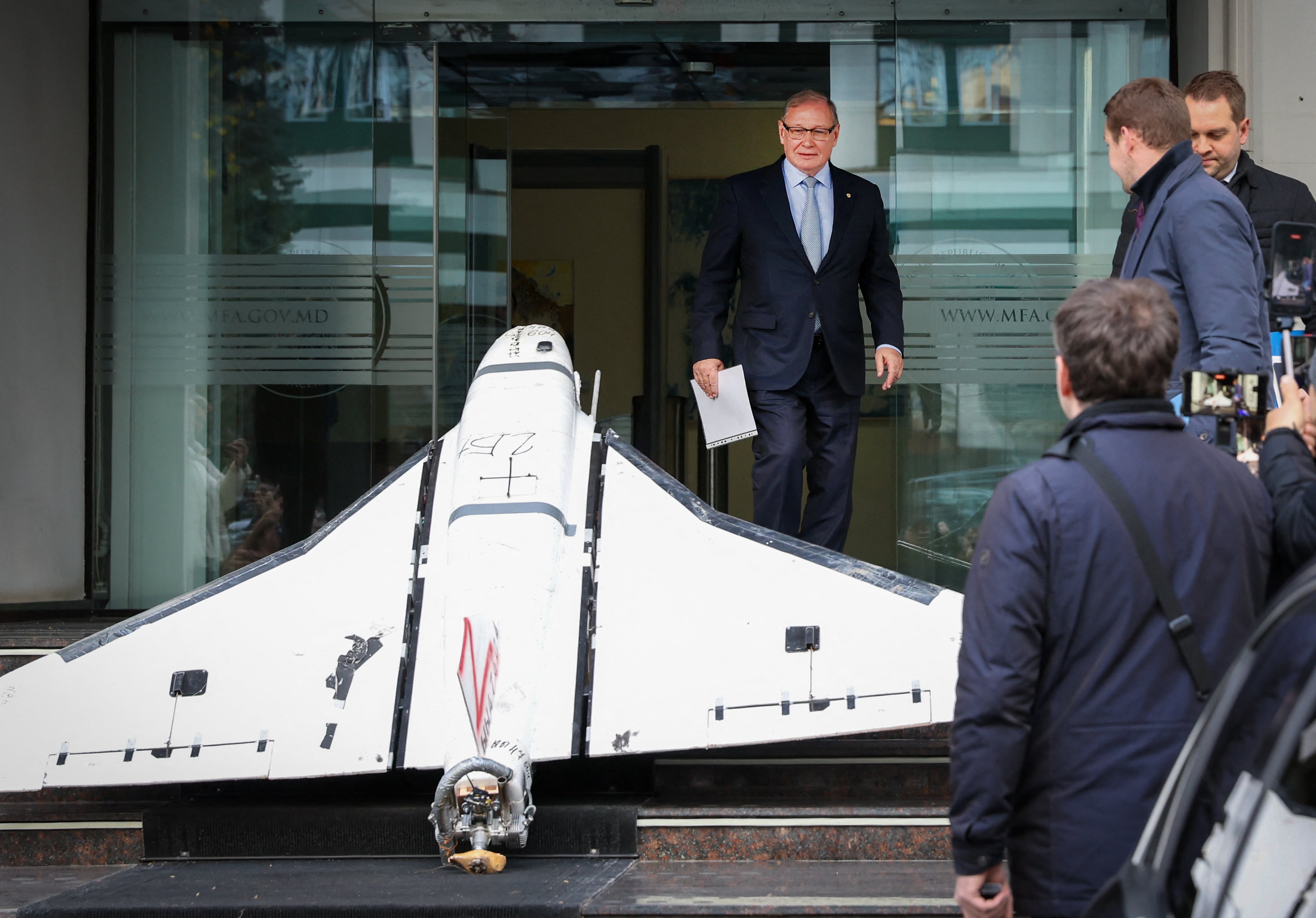 Oleg Ozerov (centro), embajador de la Federación de Rusia en Chisináu, observa un dron «Gerbera» de fabricación rusa recuperado por la policía moldava el 25 de noviembre de 2025 y exhibido en la escalinata de entrada del Ministerio de Asuntos Exteriores (MAEIE) de Moldavia en Chisináu, el 26 de noviembre de 2025 (Elena Covalenco/AFP)