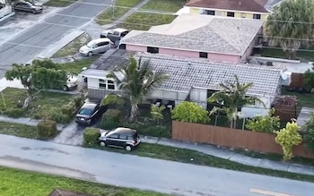 Vista aérea de un barrio con varias casas unifamiliares de una planta, calles, aceras, coches estacionados en calzadas y frente a las casas