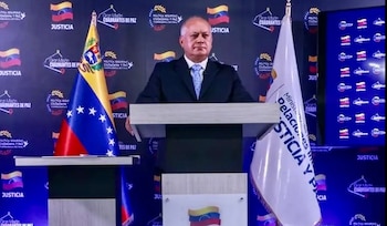 Hombre de traje y corbata en podio con la bandera de Venezuela a su izquierda y la bandera del Ministerio de Justicia y Paz a su derecha, frente a un fondo azul