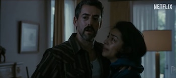 Hombre con barba abraza a mujer de cabello oscuro con lágrimas en el rostro, en interior con logotipo de Netflix en la esquina superior derecha