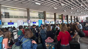 Multitud de personas dentro de un terminal de aeropuerto con mostradores de LATAM y equipaje, bajo un techo reticulado con luces