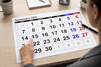 Un calendario impreso de septiembre de 2026 sobre un escritorio, con una mano que señala el día 15 y un bolígrafo a la derecha.